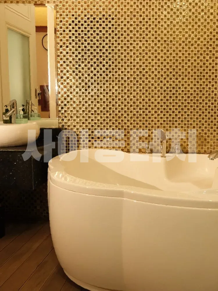 금색 모자이크 타일 벽과 하얀색 욕조가 있는 욕실